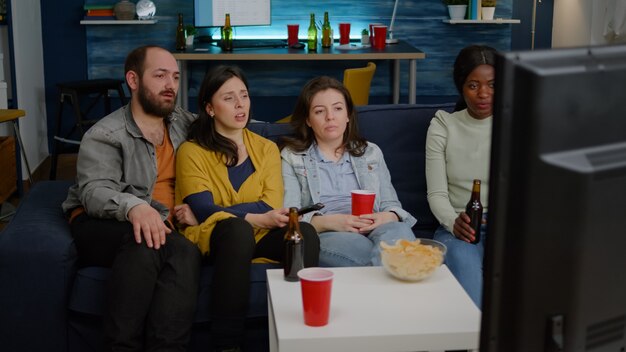 Multiracial friends changing channels on television until find funny movie